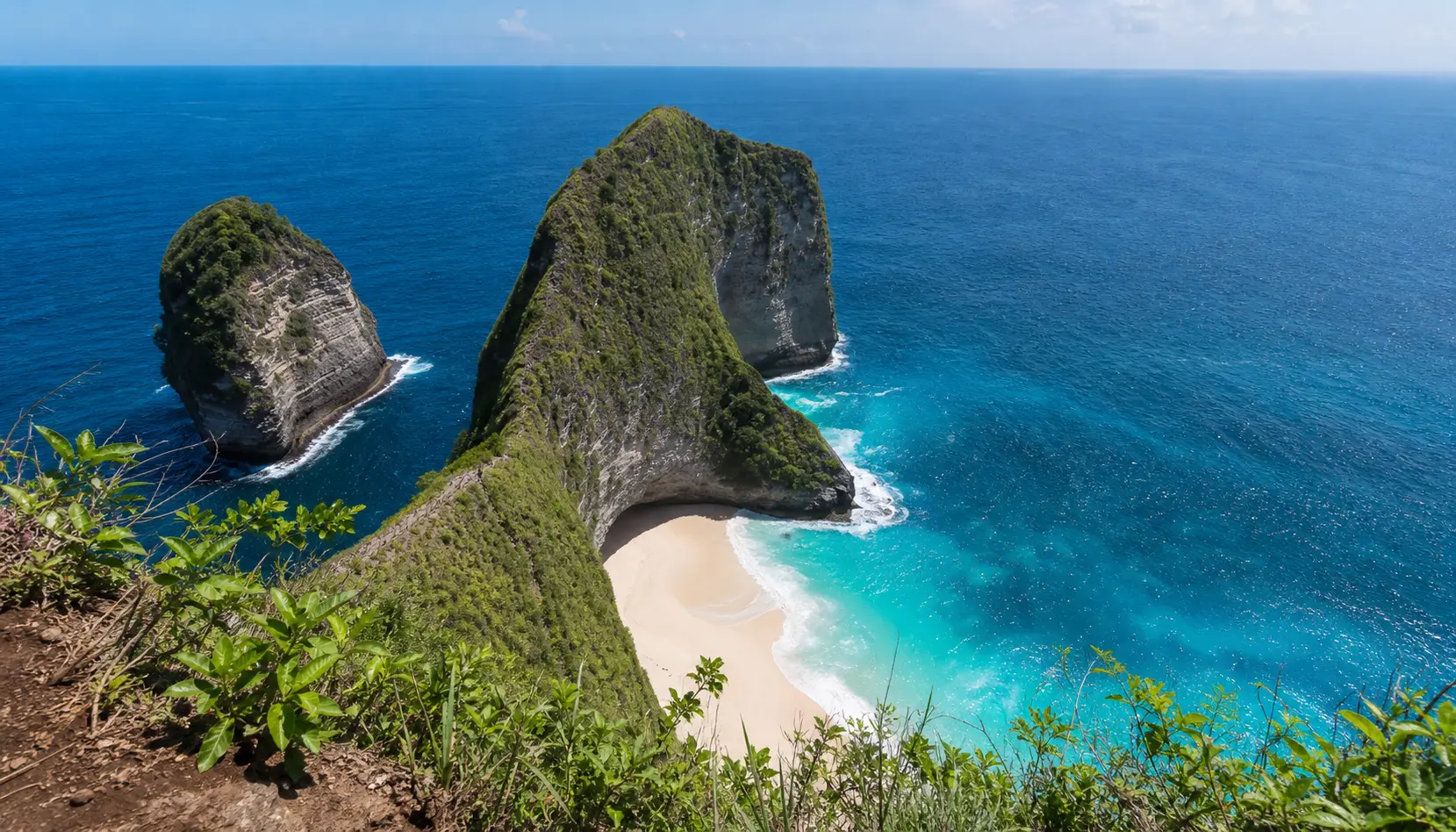 Kelingking Beach on Nusa Penida seen from the clifftop, the green headland shaped like a dinosaur's head above a curve of white sand and turquoise water